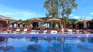 Un espace aménagé au bord de la piscine, avec des chaises longues et des parasols, le tout baigné par un ciel d’un bleu limpide.