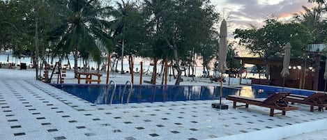 A pool area with tiled flooring, lounge chairs, and palm trees.