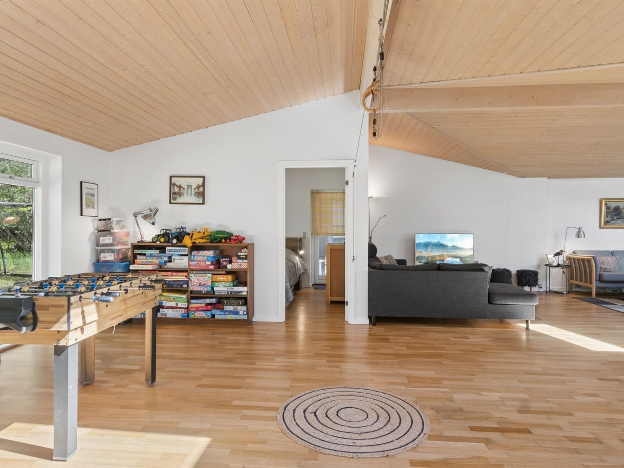 A spacious living area with a wooden ceiling, a foosball table, a sofa, and a television.