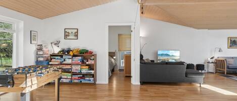 A spacious living area with a wooden ceiling, a foosball table, a sofa, and a television.