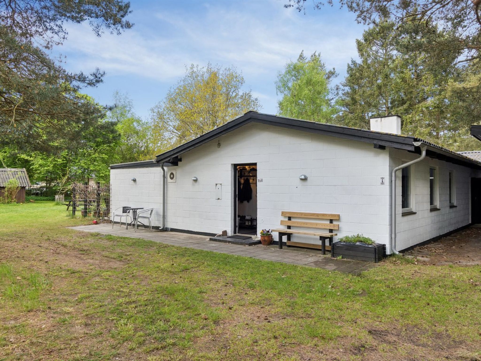 Een gelijkvloers gebouw met een witte gevel, een houten bankje buiten en een kleine tuin.