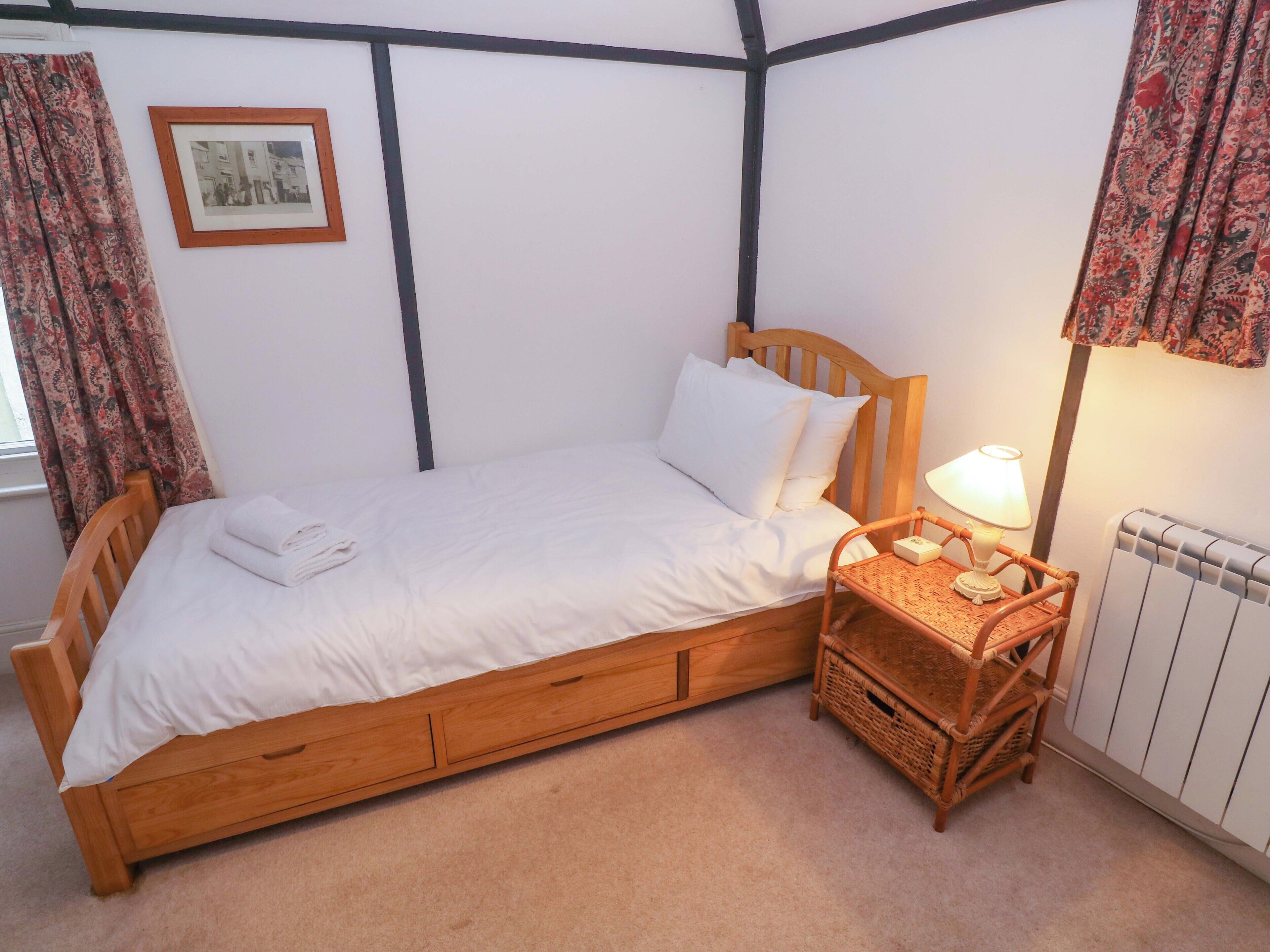 A single wooden bed with white bedding, a bedside lamp, and a wicker nightstand.