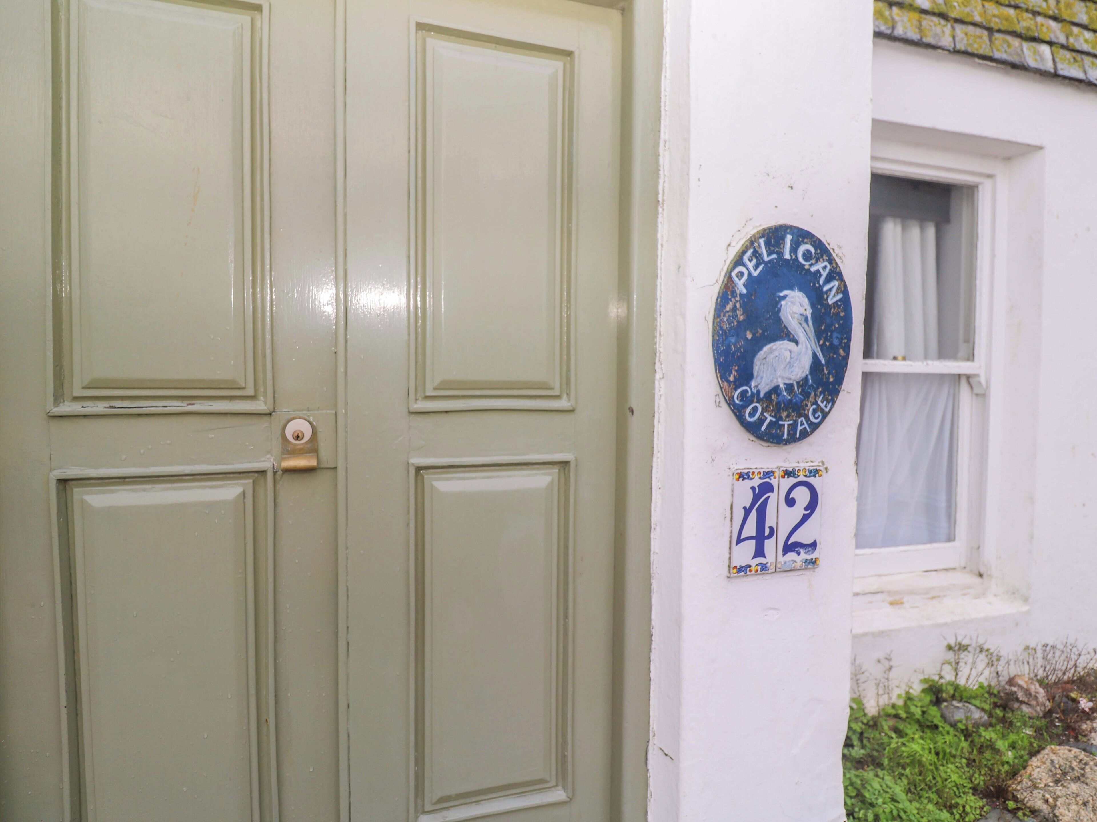 Une porte verte avec un trou de serrure, une plaque bleue ornée d’un coq blanc et une petite fenêtre avec des rideaux blancs.