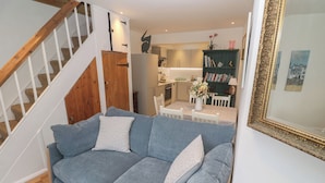 A living room with a blue sofa, a staircase, a kitchen, and a dining area. - Pelican Cottage (St Ives)