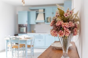 A kitchen with light blue cabinets, a dining table with chairs, and a vase with pink flowers on the table. - Apartment 'Oasi degli Dei' with Private Terrace, Wi-Fi and Air Conditioning (Santa Maria del Focallo)