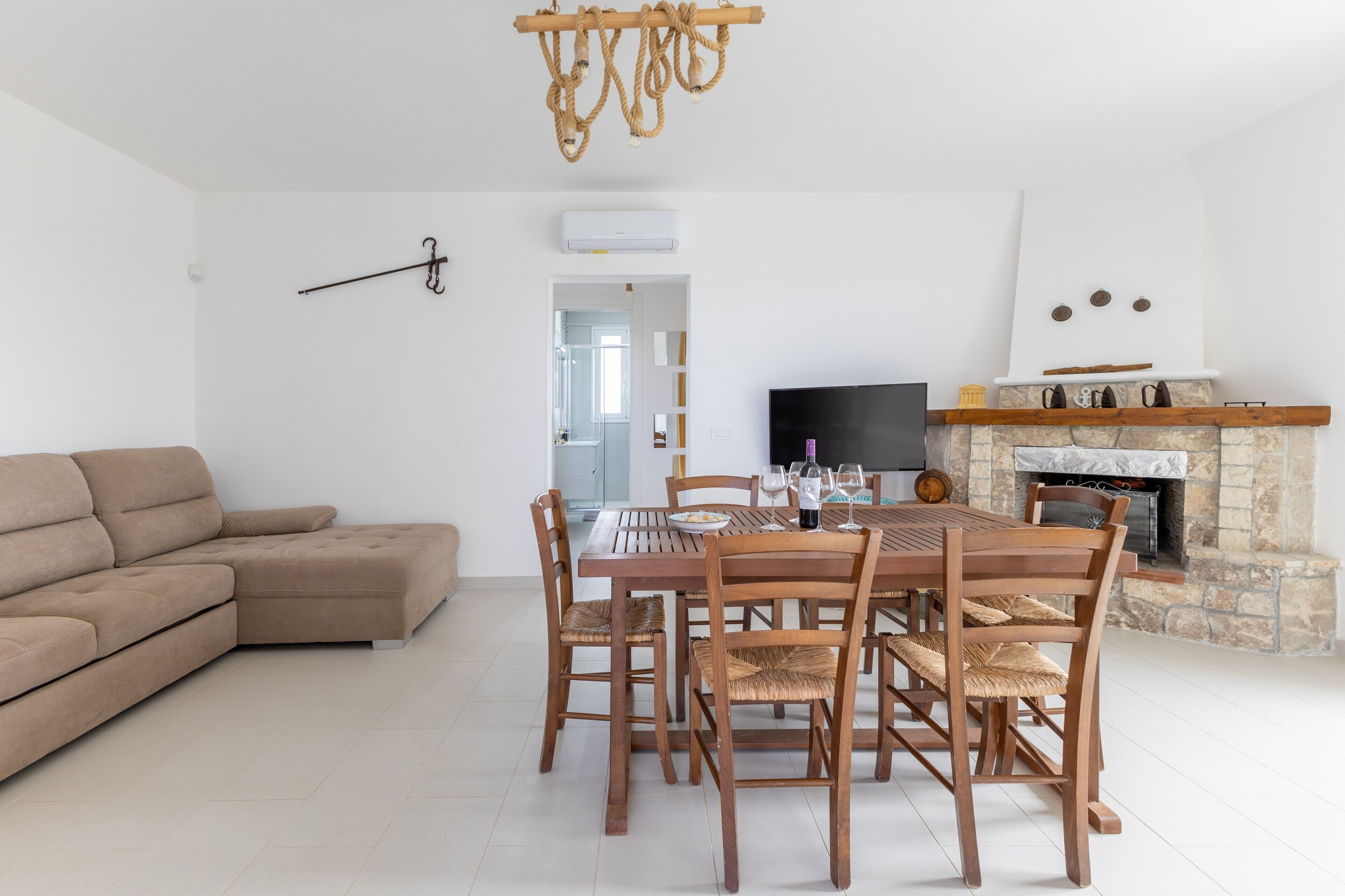 A modern living room with a sectional sofa, a wooden dining table with chairs, a fireplace, and a television.