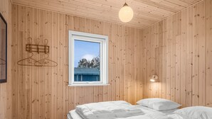 Une pièce aux murs lambrissés, une fenêtre donnant sur des arbres, deux lits avec du linge de lit blanc et un luminaire suspendu.