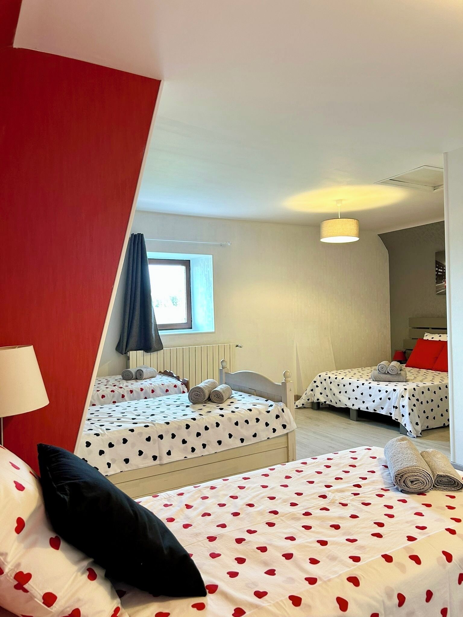 A hotel room with two beds, each with heart-patterned bedding, a window with curtains, a radiator, and a ceiling light.