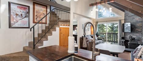 A modern kitchen with a stainless steel sink, wooden countertops, and a unique faucet. A staircase with a wooden railing leads to a loft area.