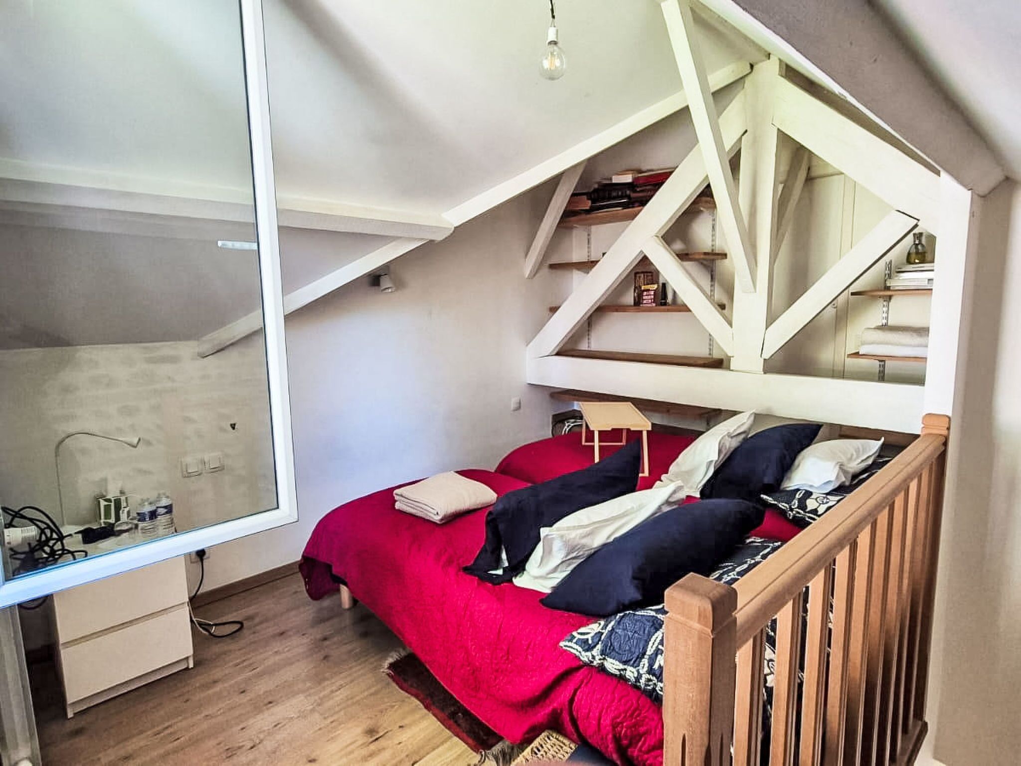 Une chambre avec un plafond en pente, un lit avec une literie rouge, une tête de lit en bois et un petit bureau avec une chaise.