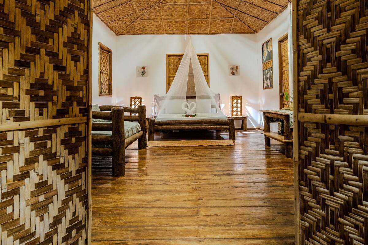 A room with a thatched roof, wooden floors, a bed with a canopy, and woven wooden walls.