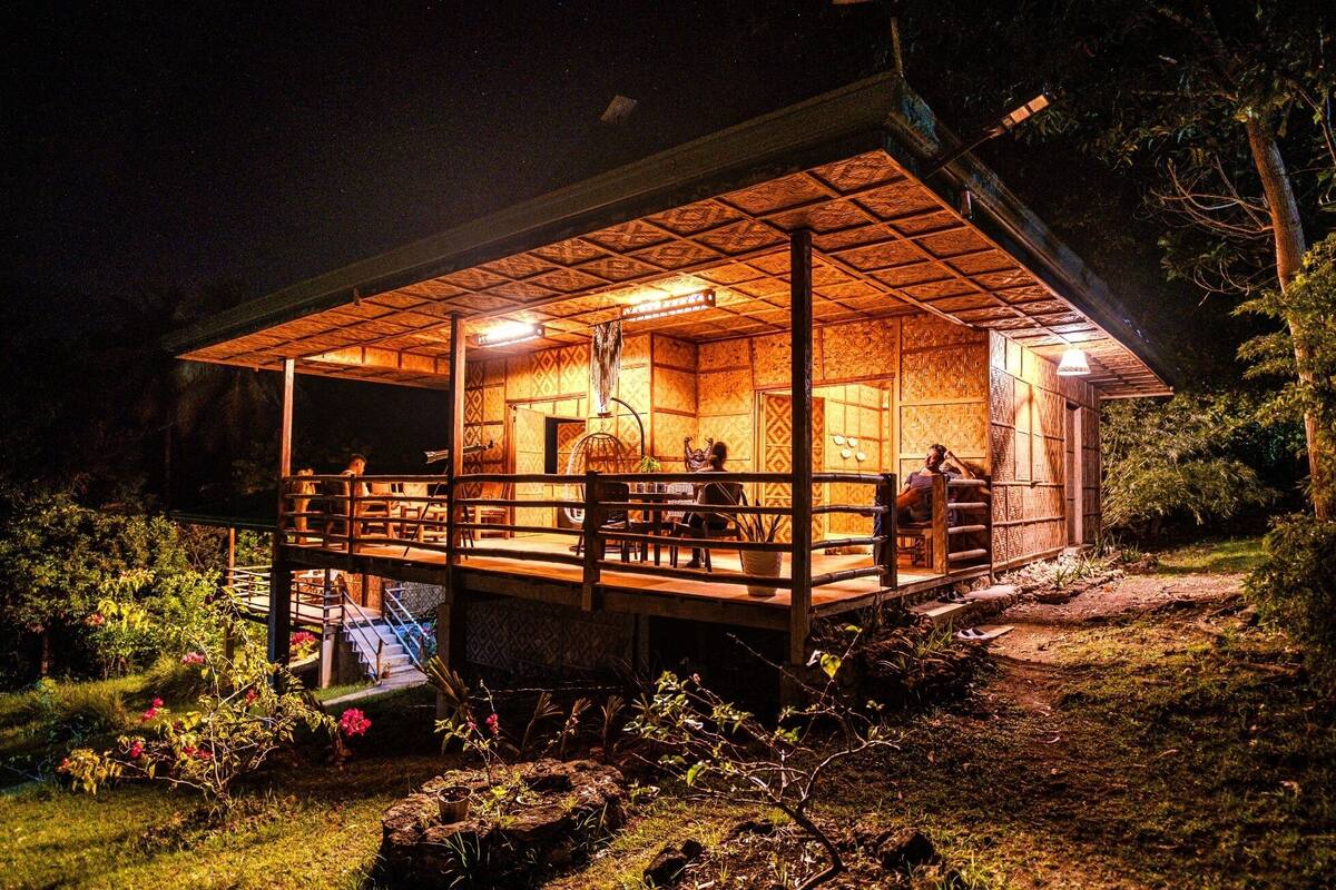 A wooden cabin with a covered deck, a staircase leading to the entrance, and a garden area with rocks and plants.