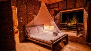 A wooden bed with a canopy in a room with patterned walls and a view of the outdoors. - om horizon ecoresort (Loay)