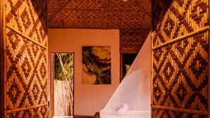 A room with a wooden floor, a bed with a mosquito net, a ceiling fan, and a painting on the wall. - om horizon ecoresort (Loay)
