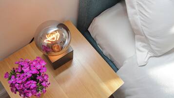 A wooden bedside table with a clear glass lamp containing a glowing light bulb and a small flower arrangement.