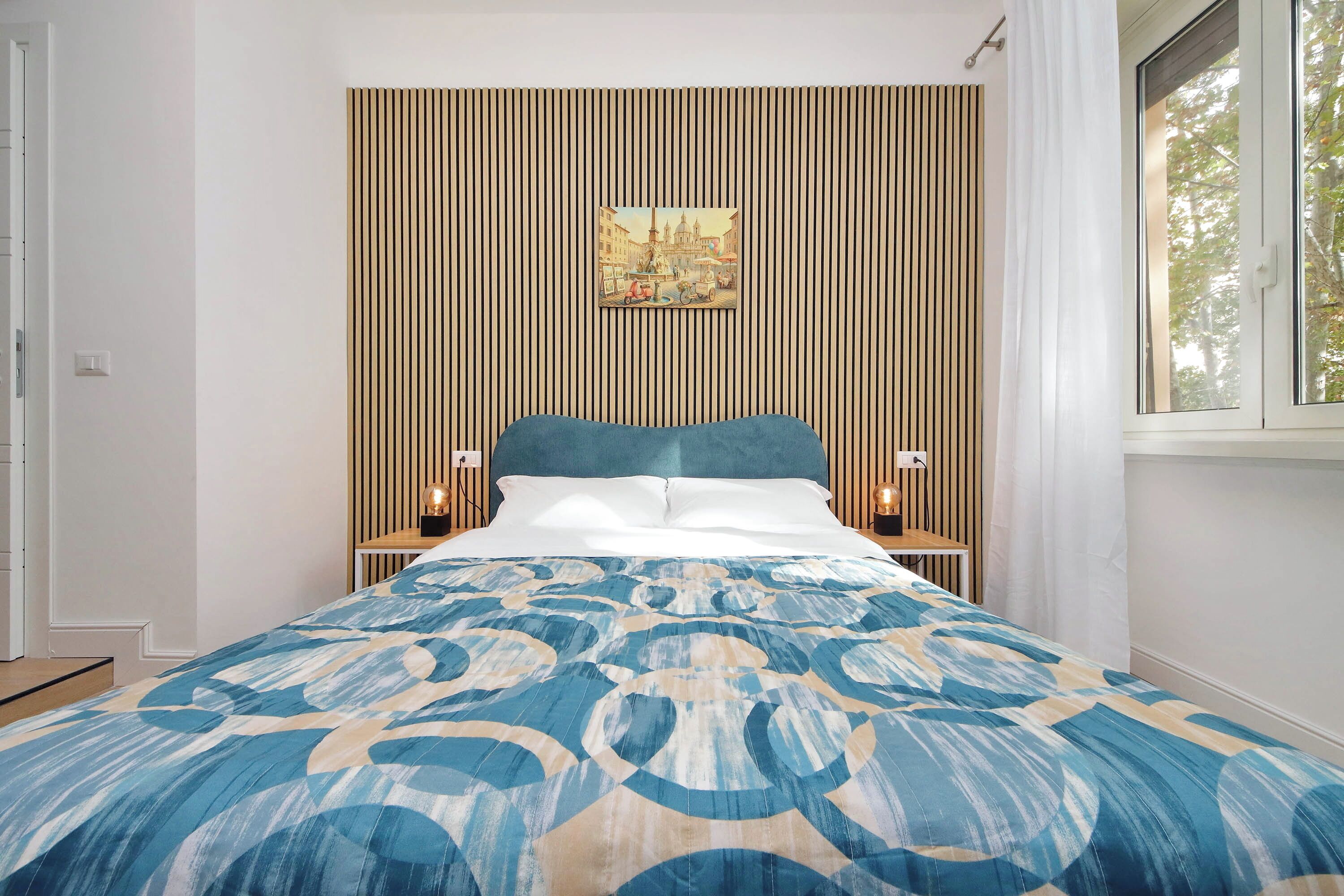 Un dormitorio con cama, un cuadro colgado en la pared y una ventana con cortinas.