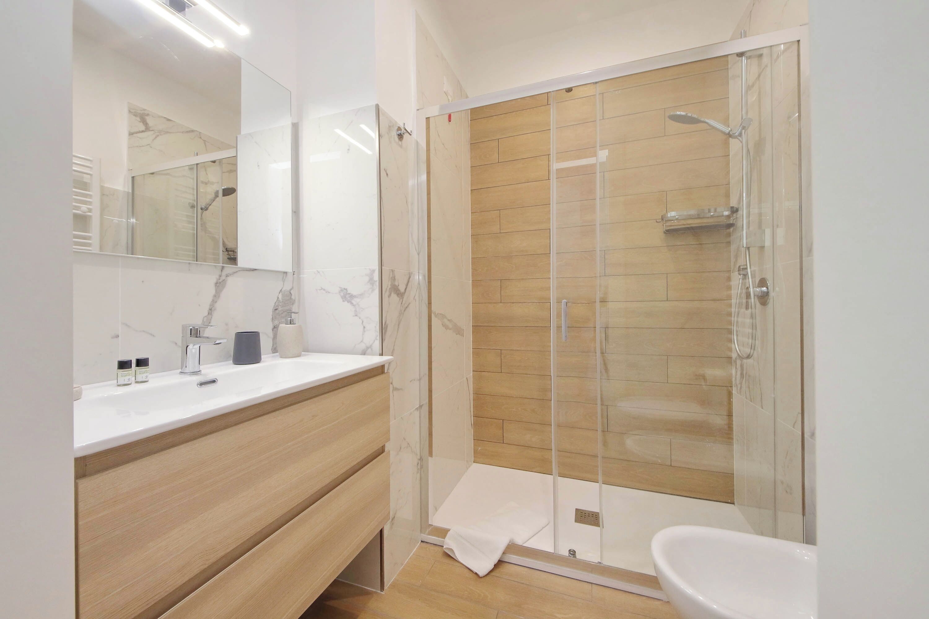 Une salle de bain moderne avec une douche à parois de verre, un meuble-lavabo en bois et un grand miroir.