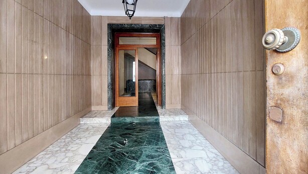 A hallway with marble flooring, a wooden door with a metal handle, and a hanging light fixture. - Foro Italico Guesthouse (Rome)