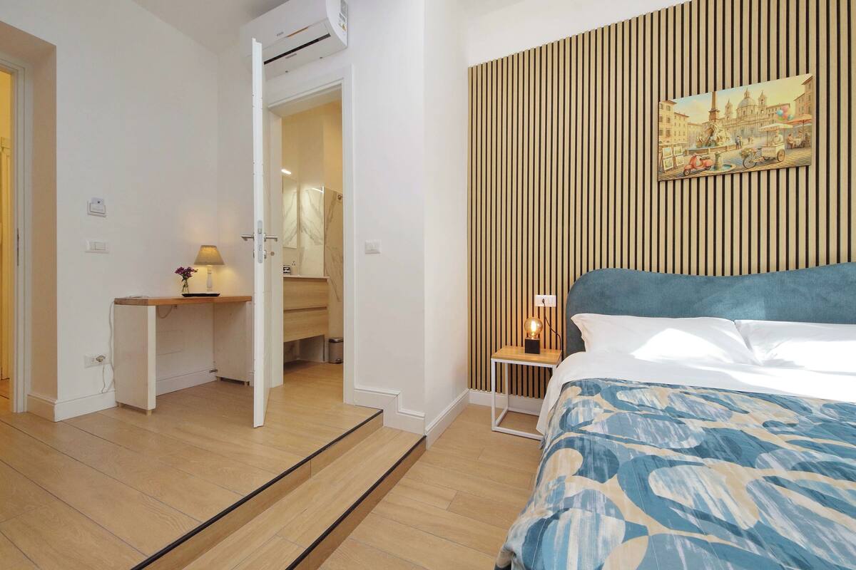 A bedroom with a bed, a desk, and a painting on the wall.