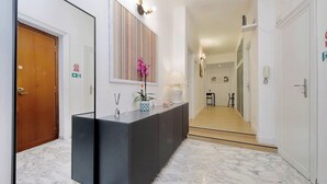 A hallway with a reception desk, a mirror, a potted plant, and a patterned wall. - Foro Italico Guesthouse (Rome)