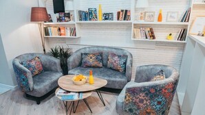 A cozy living area with a grey sofa set, a coffee table, and a bookshelf filled with books and decorative items. - Citrus Boutique Hotel (Baku)
