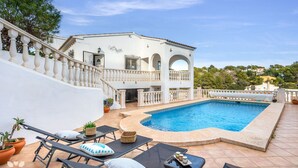 En hvid villa med swimmingpool, havemøbler og en trappe op til en balkon.