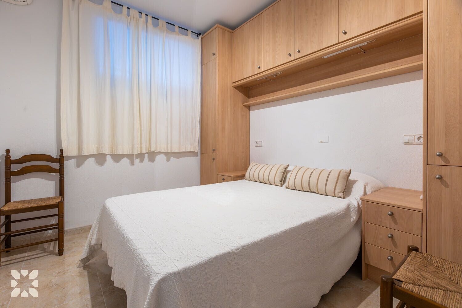 A bedroom with a bed, wooden wardrobe, and a chair.