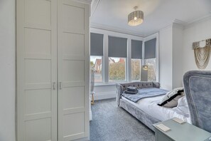 Een slaapkamer met een bed, een grijze bank, een raam met uitzicht en een witte inbouwkast.