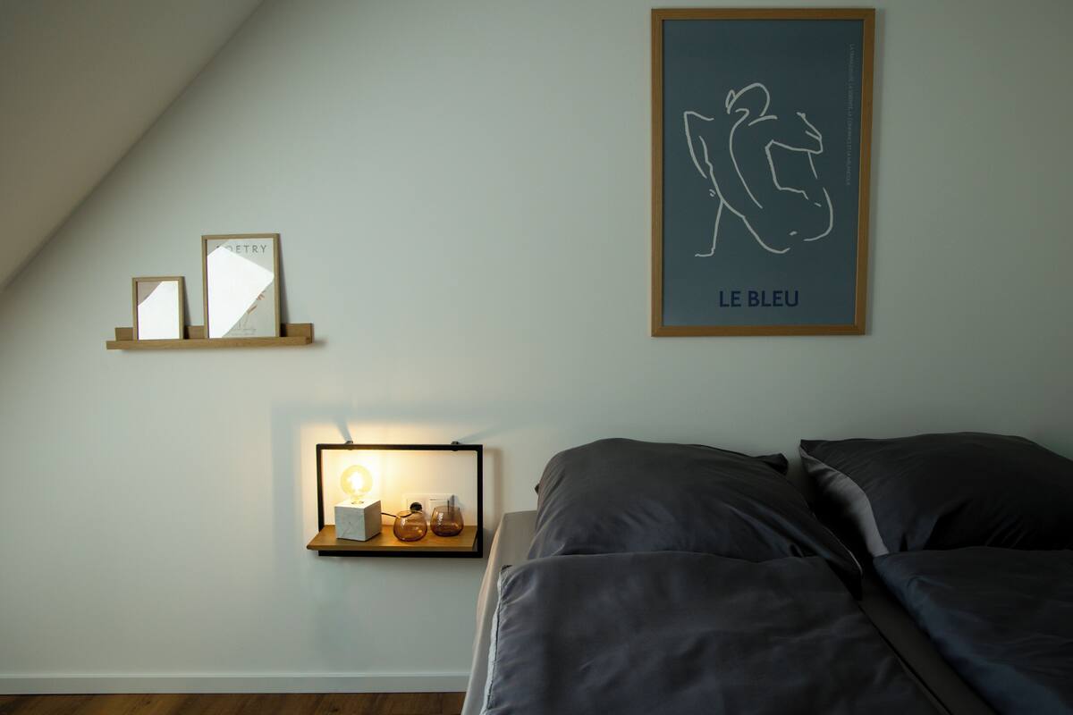 Ein Schlafzimmer mit einem Bett, einem Nachttisch mit Lampe und zwei gerahmten Bildern an der Wand.