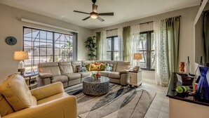 Ein geräumiges Wohnzimmer mit einer Sofagarnitur, einem Couchtisch und einem Deckenventilator.