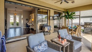 Eine Terrasse im Freien mit Korbmöbeln, einem Deckenventilator und Grillplatz.