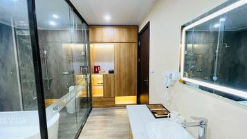Un baño moderno con cabina de ducha de vidrio, tocador de madera, espejo grande y secador de pelo en la pared.