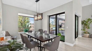 A modern dining area with a large table, grey chairs, and a hanging light fixture. - Villa 5 Modern Coastal Luxury. NEW TO RENTAL (Cape coral)