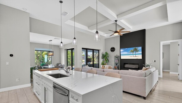 A modern kitchen with a large island, a dining area with a sofa, and a living room with a TV. - Villa 5 Modern Coastal Luxury. NEW TO RENTAL (Cape coral)