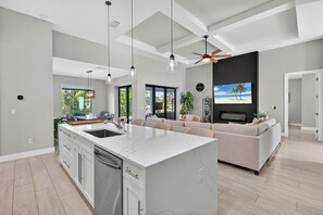 A modern kitchen with a large island, a dining area with a sofa, and a living room with a TV. - Villa 5 Modern Coastal Luxury. NEW TO RENTAL (Cape coral)