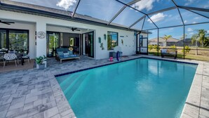A covered outdoor swimming pool with a patio area, seating, and a view of the surrounding landscape. - Villa 5 Modern Coastal Luxury. NEW TO RENTAL (Cape coral)