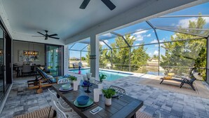 A covered patio with a pool, outdoor seating, and a dining area. - Villa 5 Modern Coastal Luxury. NEW TO RENTAL (Cape coral)