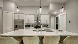 A modern kitchen with white cabinets, a large island with bar stools, and pendant lighting. - Villa 5 Modern Coastal Luxury. NEW TO RENTAL (Cape coral)