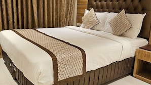 Una cama grande con cabecera capitonada, una mesita de noche de madera y un corredor de cama estampado.