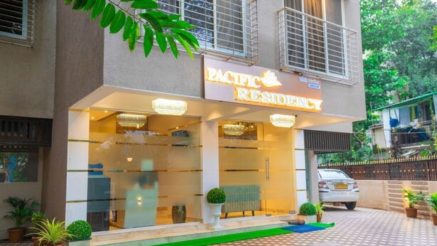 Edificio Pacific Residency con fachada de vidrio, felpudo verde de entrada y plantas en macetas.