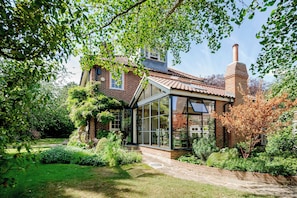 A house with a brick exterior, a glass conservatory, and a garden with various plants. - Beautiful Family Home With Garden & Pool - Wimbledon (London)