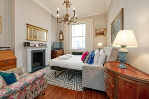Une chambre d’hôtel comprenant un lit, un canapé, une commode, une télévision, une cheminée et un lustre.