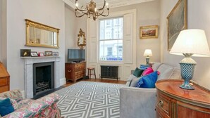 A living room with a fireplace, a sofa, a television, and a chandelier. - Traditional 1 Bed Apartment, Pimlico (London)