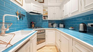 Cucina con mobili bianchi, piastrelle blu, bollitore in acciaio inossidabile e tostapane.