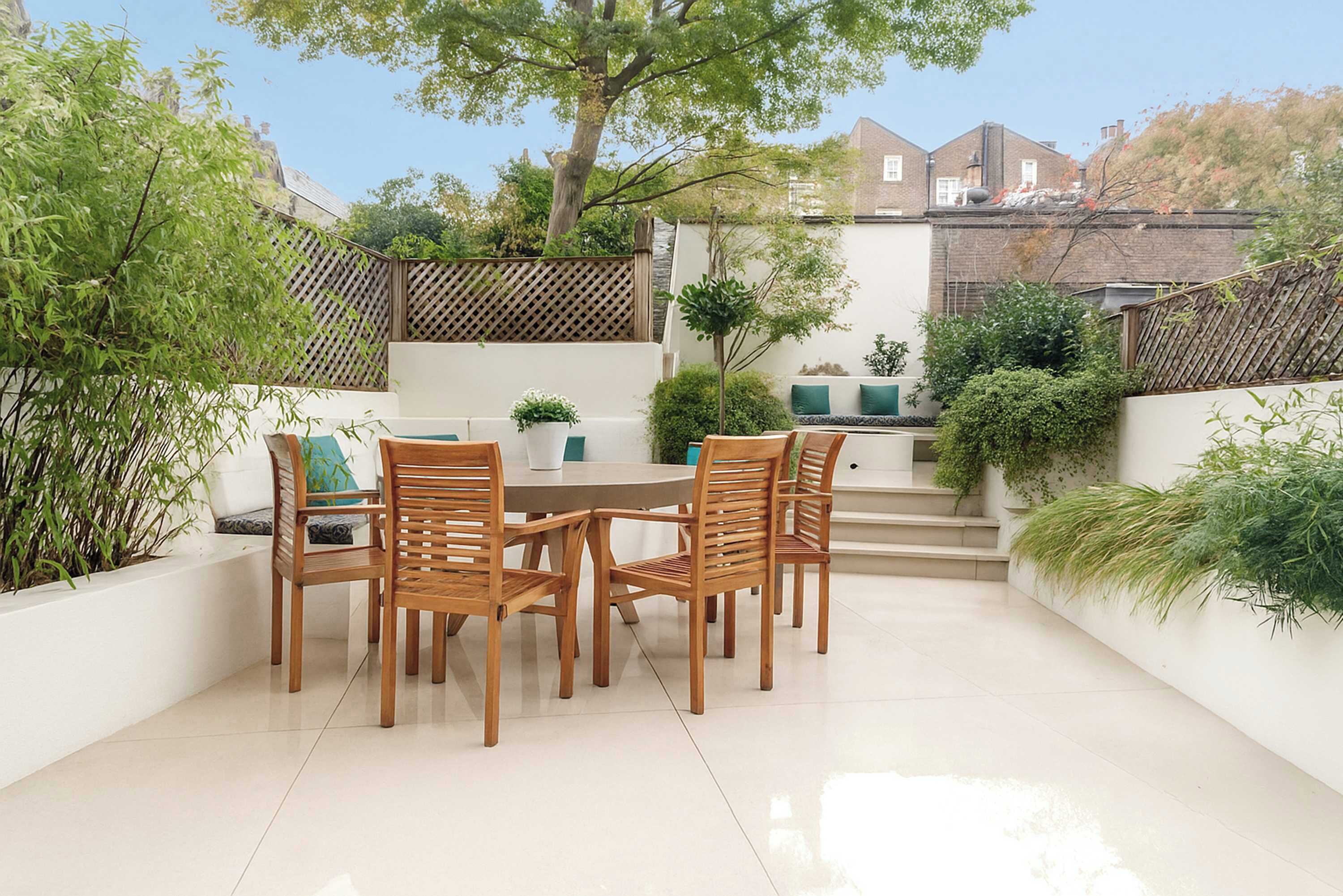Een terras met een ronde tafel en houten stoelen, omringd door witte muren en potplanten.