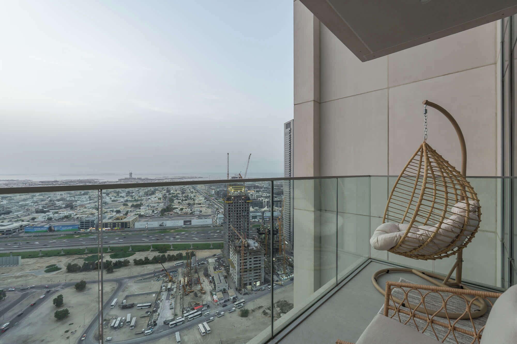 Un balcón en un edificio alto con una silla colgante y vistas a un paisaje urbano con obras en construcción.
