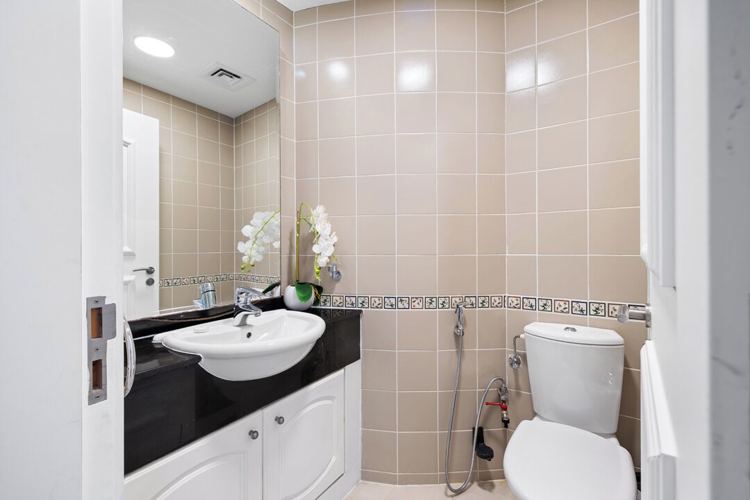A bathroom with a white sink, black countertop, beige tiles, a toilet, and a shower.