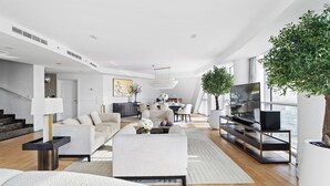 A modern living room with a sofa, coffee table, and TV stand. There is a staircase leading to another level, and a large window providing natural light. - Penthouse Private Pool and Yacht Views (Dubai)