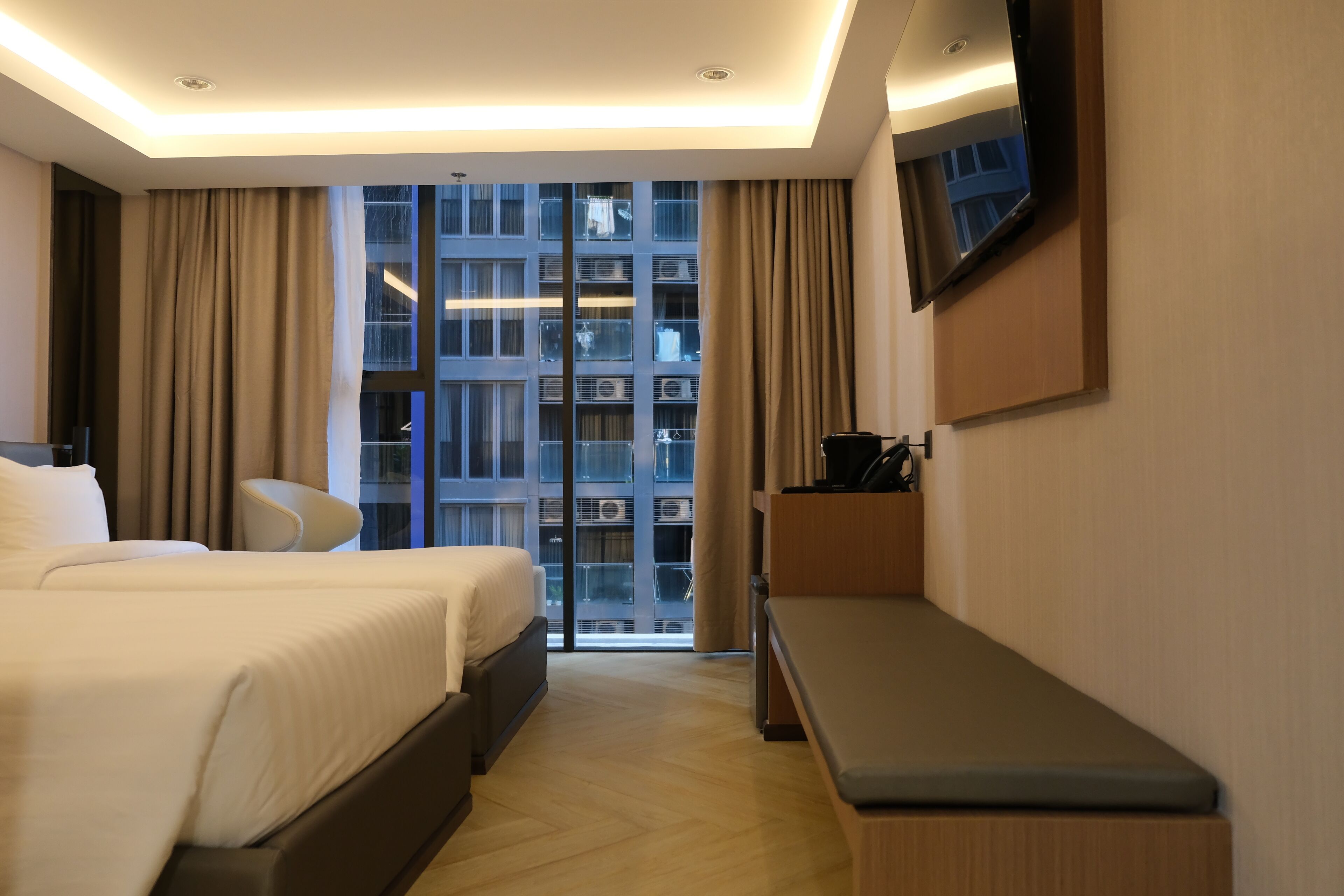 A hotel room with a bed, a desk, a chair, a TV, and a large window with a view of a building.