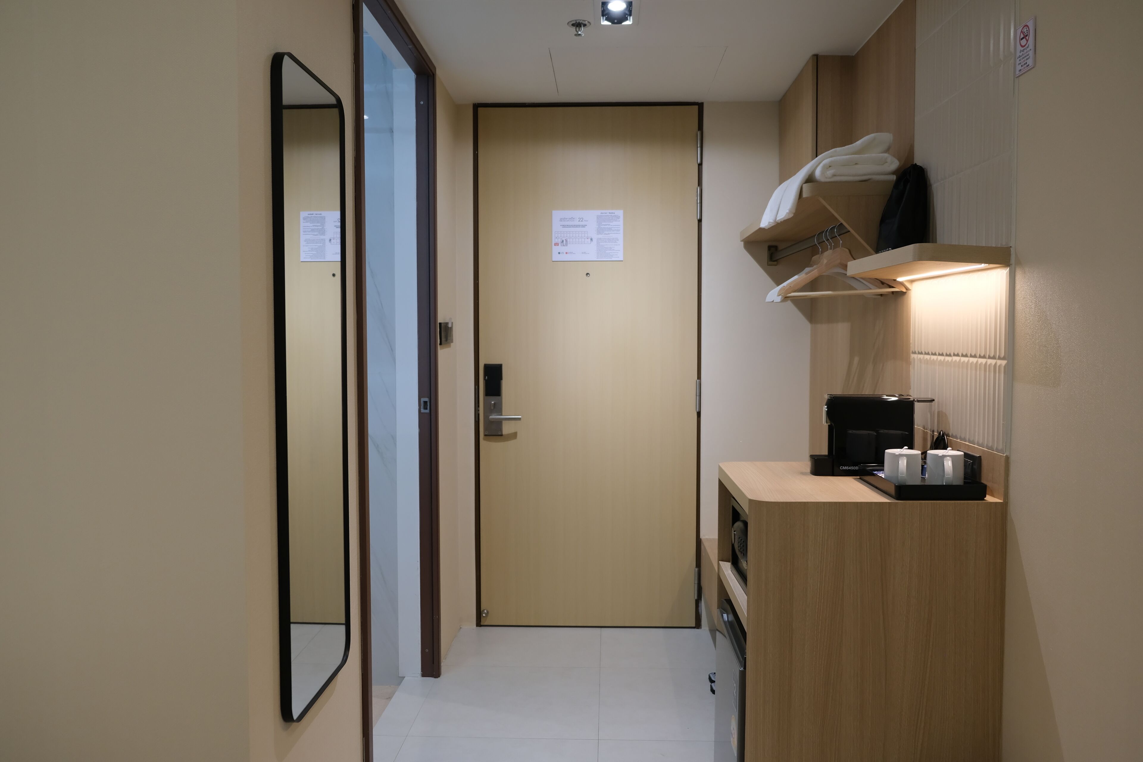 Habitación de hotel con escritorio de madera, cafetera, perchero y puerta con un aviso.